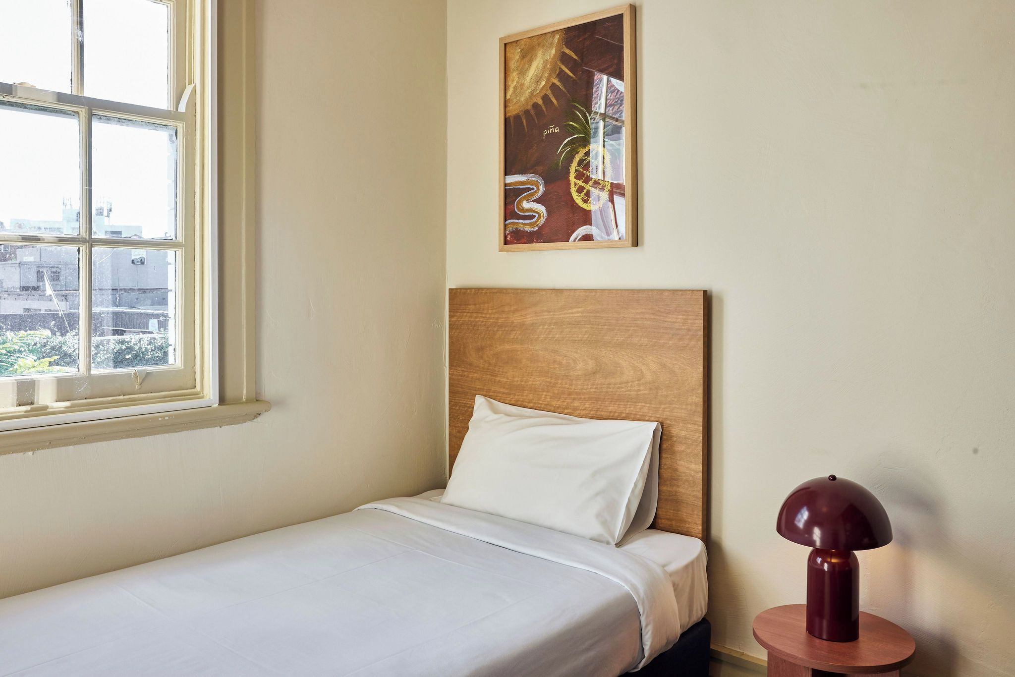A single bed with a wooden headboard, a white pillow, and a round table with a lamp.
