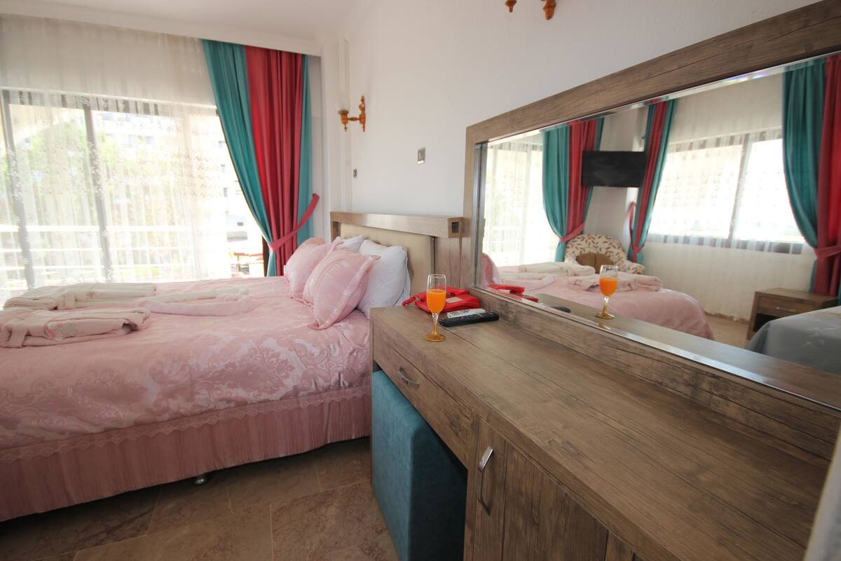 A bedroom with a large bed, a wooden dresser, a mirror, and a window with curtains.