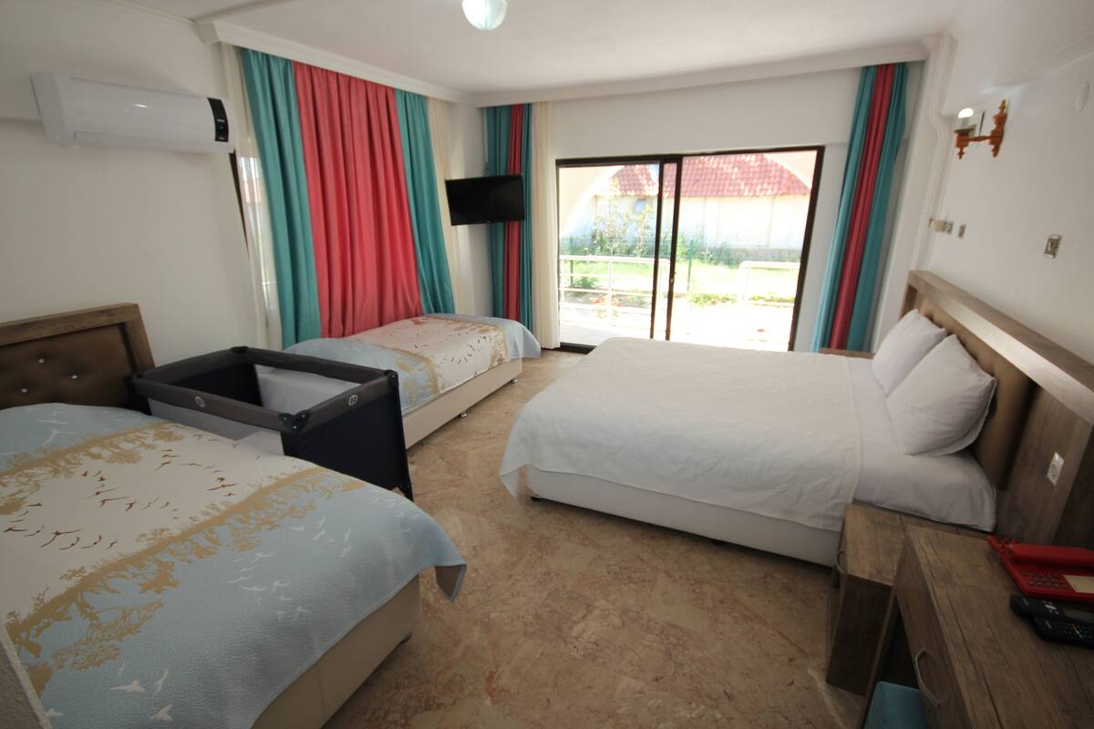 A hotel room with two beds, a TV, a desk with a phone, and a sliding glass door to the outside.