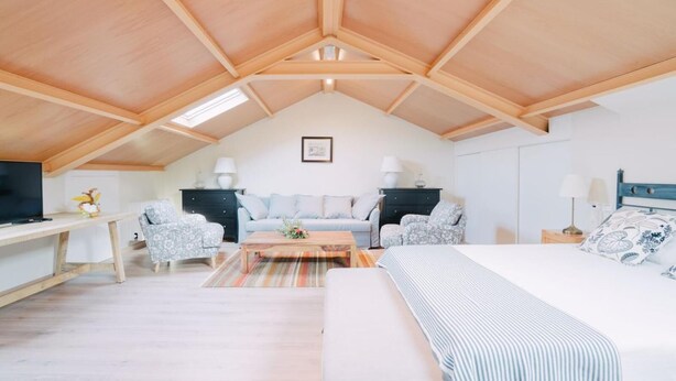 A cozy loft bedroom with a sloped ceiling, a large bed, a desk, and two armchairs. - O Cruceiro (Boiro)