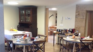 A dining area with wooden tables and chairs, a cabinet, and a kitchen area with appliances. - O Cruceiro (Boiro)