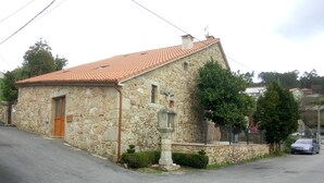 A stone building with a tiled roof, a wooden door, and a small garden area. - O Cruceiro (Boiro)