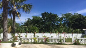 A paved driveway leading to a white fence with decorative balusters, surrounded by lush greenery and palm trees. - Summer Splash Resort (Gingoog)