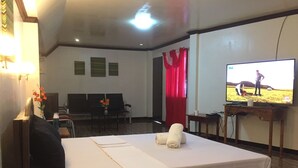 A hotel room with a bed, a desk, a television, and a window with red curtains. - Summer Splash Resort (Gingoog)