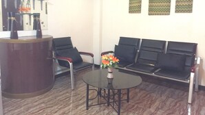 A reception area with a reception desk, two black chairs, a small table with a vase of flowers, and three patterned wall decorations. - Summer Splash Resort (Gingoog)