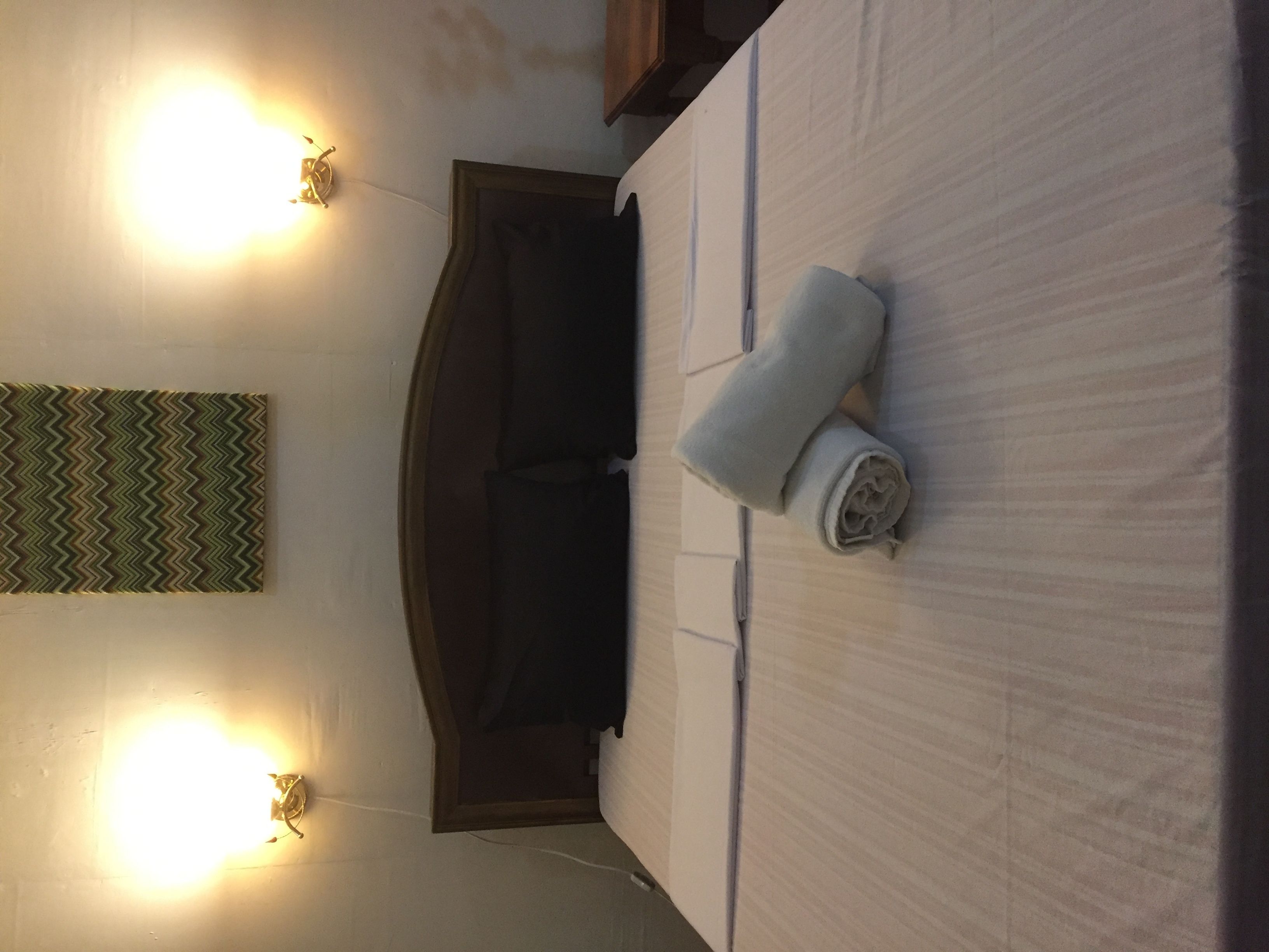 Una habitación de hotel con una cama, cabecera y dos luces fijadas a la pared.