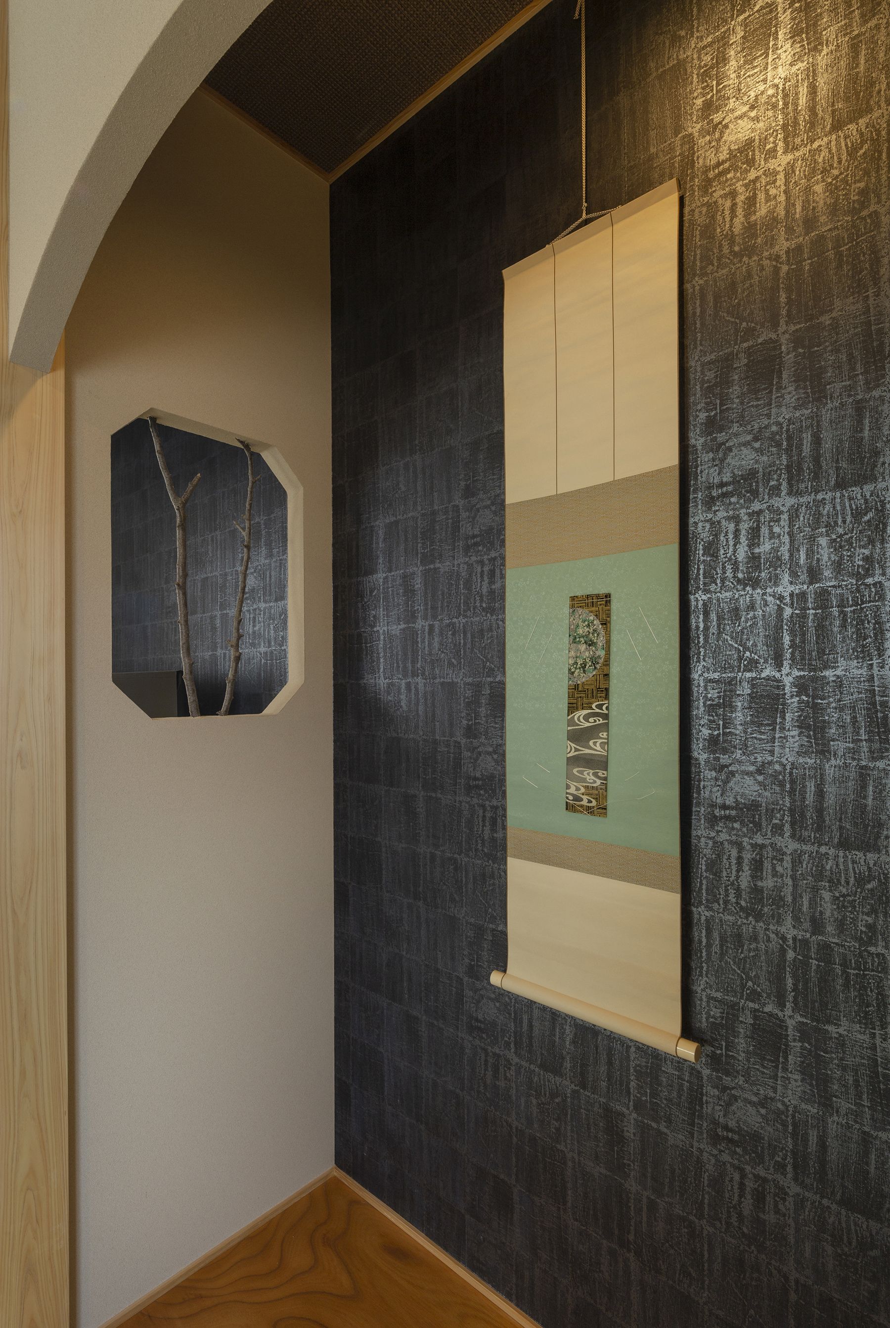A hallway with a textured dark wall, a wooden floor, and a framed artwork with a geometric design.