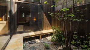 A modern building with large glass windows, a wooden deck, and a small garden area with rocks and plants. - hisashi (Kyoto)