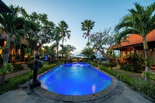 Piscina rodeada por plantas tropicais e palmeiras, com uma estátua em primeiro plano.