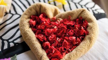 Un cuenco con forma de corazón lleno de flores rojas sobre una cama con un cojín a rayas de cebra.