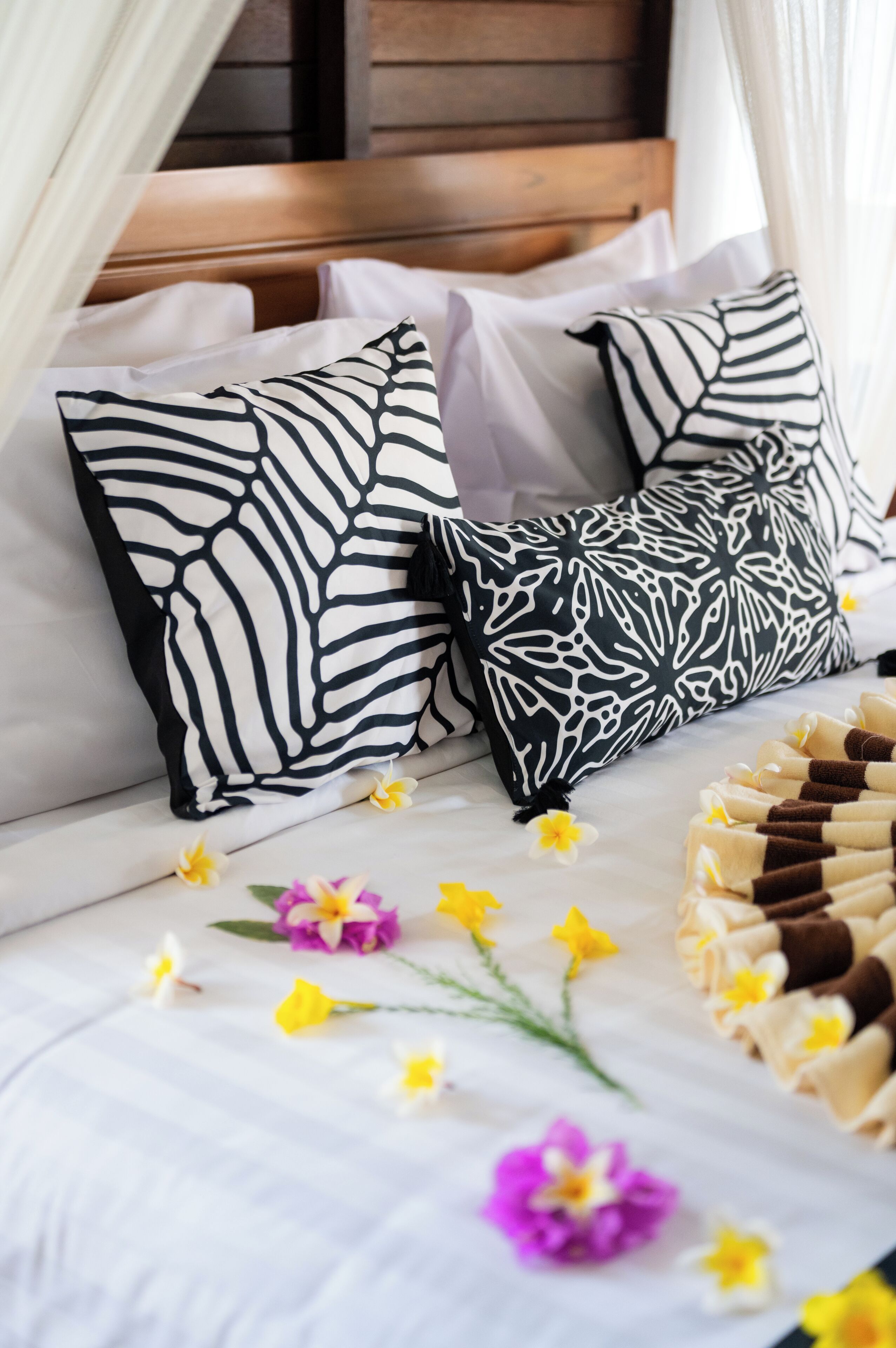A bed with white bedding, two patterned pillows, and scattered flowers.