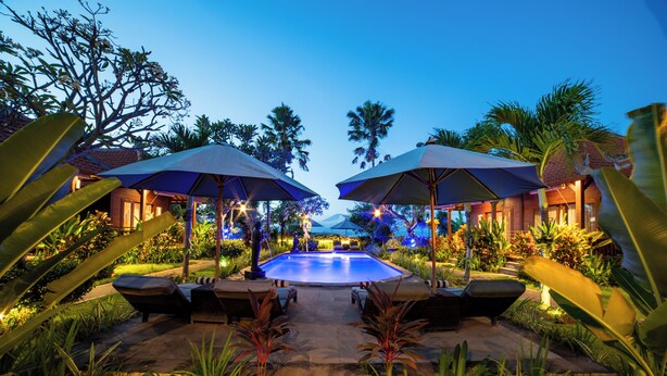 A pool area with lounge chairs and umbrellas, surrounded by tropical plants and palm trees. - D'Puncak Villas Lembongan (Lembongan Island)