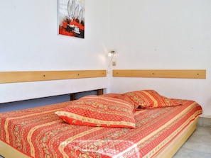 Una cama con una colcha y almohadas estampadas en rojo, un cabecero de madera y una lámpara fijada a la pared.