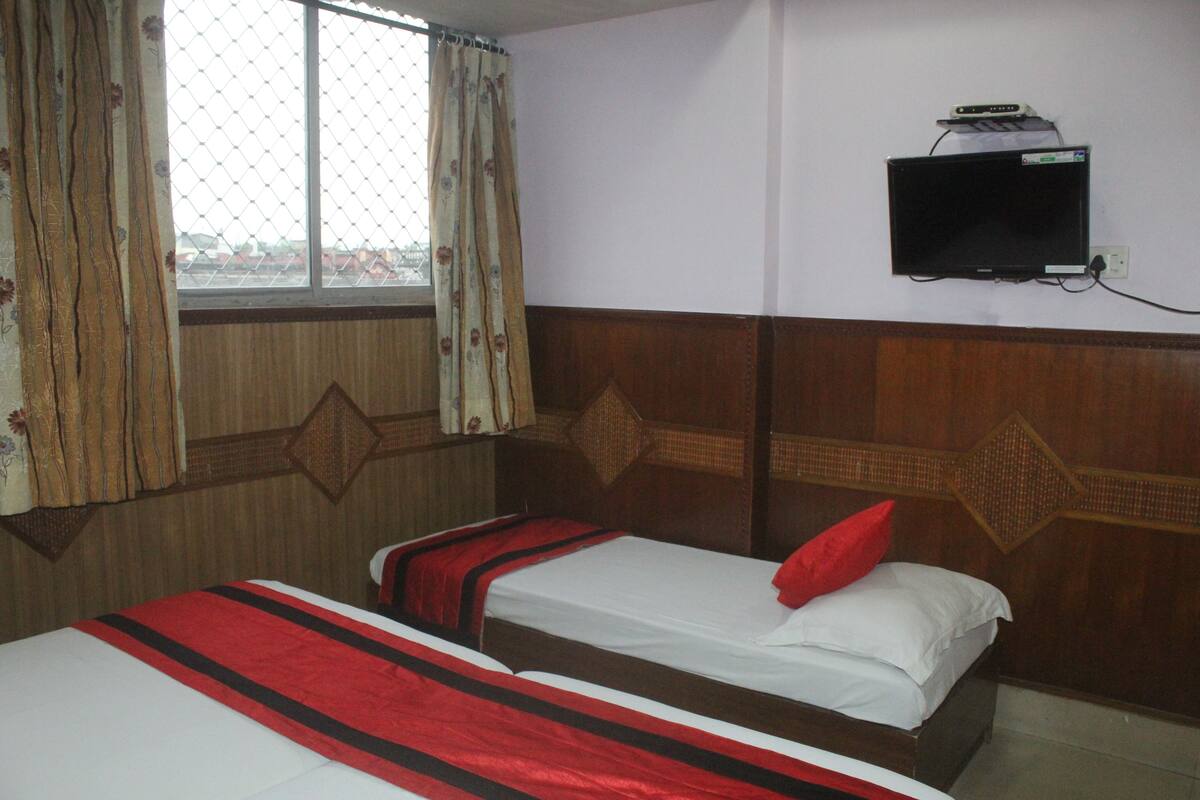 A hotel room with two beds, a TV mounted on the wall, and a window with curtains.