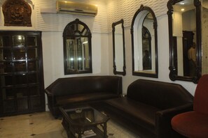A room with a dark brown leather sofa, a glass coffee table, and a red chair. There are multiple mirrors on the walls, and a wooden cabinet with glass doors.