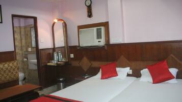 A hotel room with a large bed, a mirror, a clock, and an air conditioning unit.