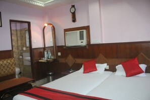 A hotel room with a large bed, a mirror, a clock, and an air conditioning unit.