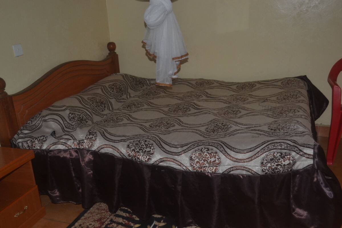 A bed with a patterned bedspread, a wooden headboard, and a red chair.