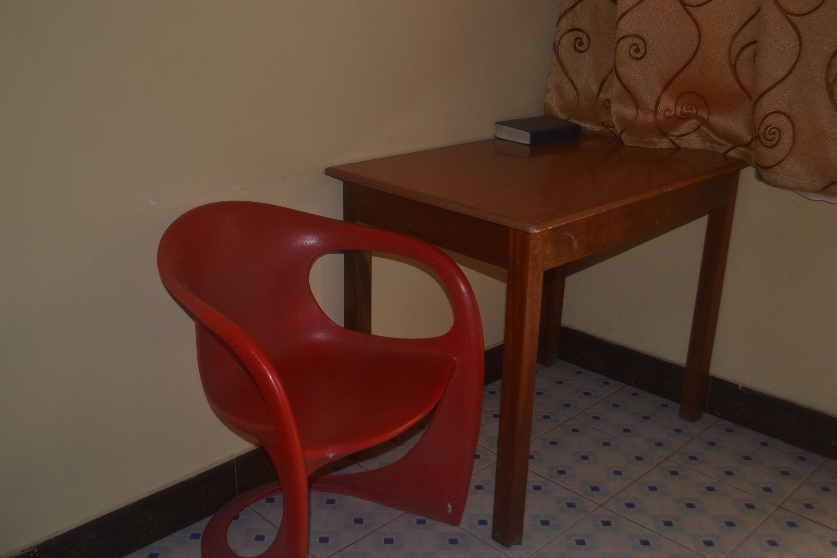 Une chaise en plastique rouge est placée à côté d’une table en bois sur laquelle se trouve un livre.