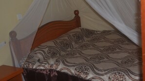 Una cama con cabecera de madera, una colcha estampada y una mosquitera.