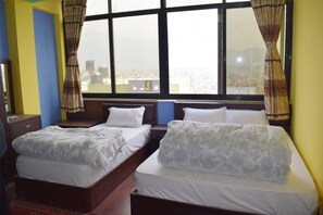A hotel room with two beds, a large window with curtains, and a view of a cityscape. - Hotel Om (Kathmandu)