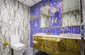 A bathroom with a white toilet, gold vanity, and blue-tiled walls. - DJ Suites Blackpool (Blackpool)