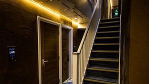 A hotel hallway with a wooden door labeled "108," a carpeted staircase, and a digital welcome sign.