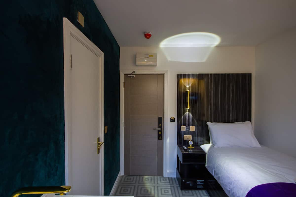 A hotel room with a bed, bedside table, and a door leading to a bathroom.