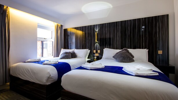 A hotel room with two beds, a large window, and a modern ceiling light.