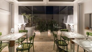 An outdoor dining area with tables and chairs, potted plants, and a glass partition. - Iulius Suite & spa (Conversano)