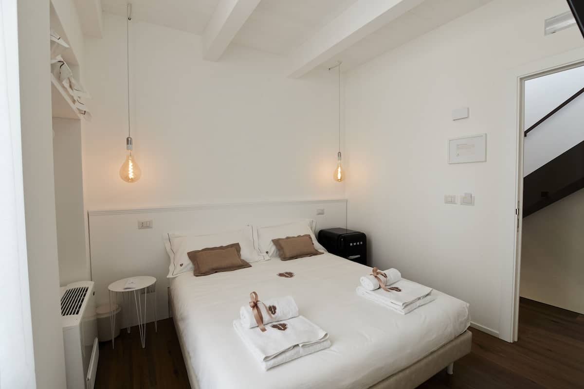 Habitación de hotel ordenada con una cama grande, dos mesitas de noche, una mesita redonda pequeña y una maleta negra.