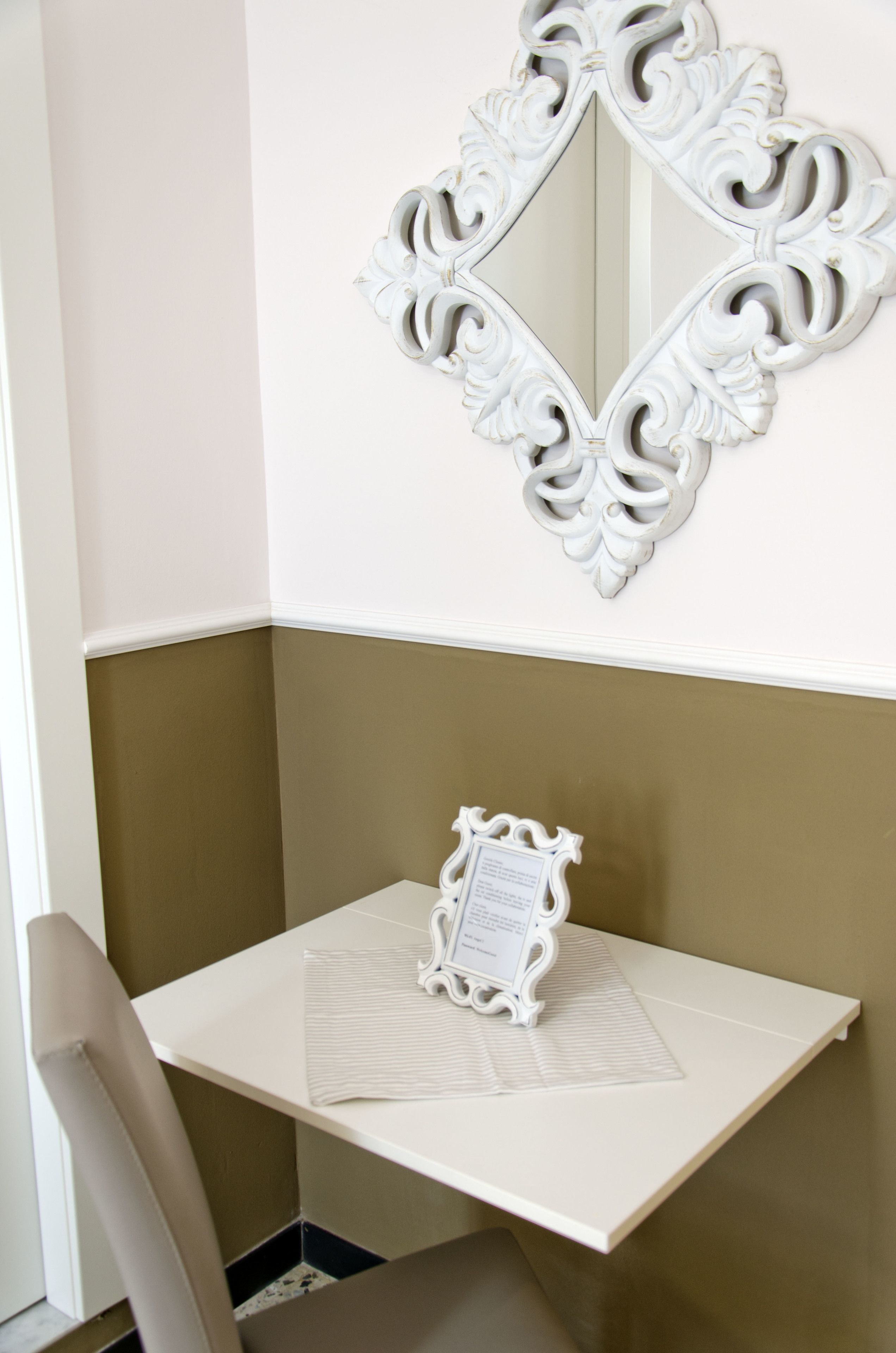 A corner room with a white table, a chair, and a decorative mirror on the wall.