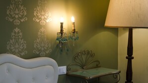A room with a green wall, a white upholstered headboard, a small table with a glass top, and two wall-mounted lamps with green glass shades. - Affittacamere Angel 2 (La Spezia)