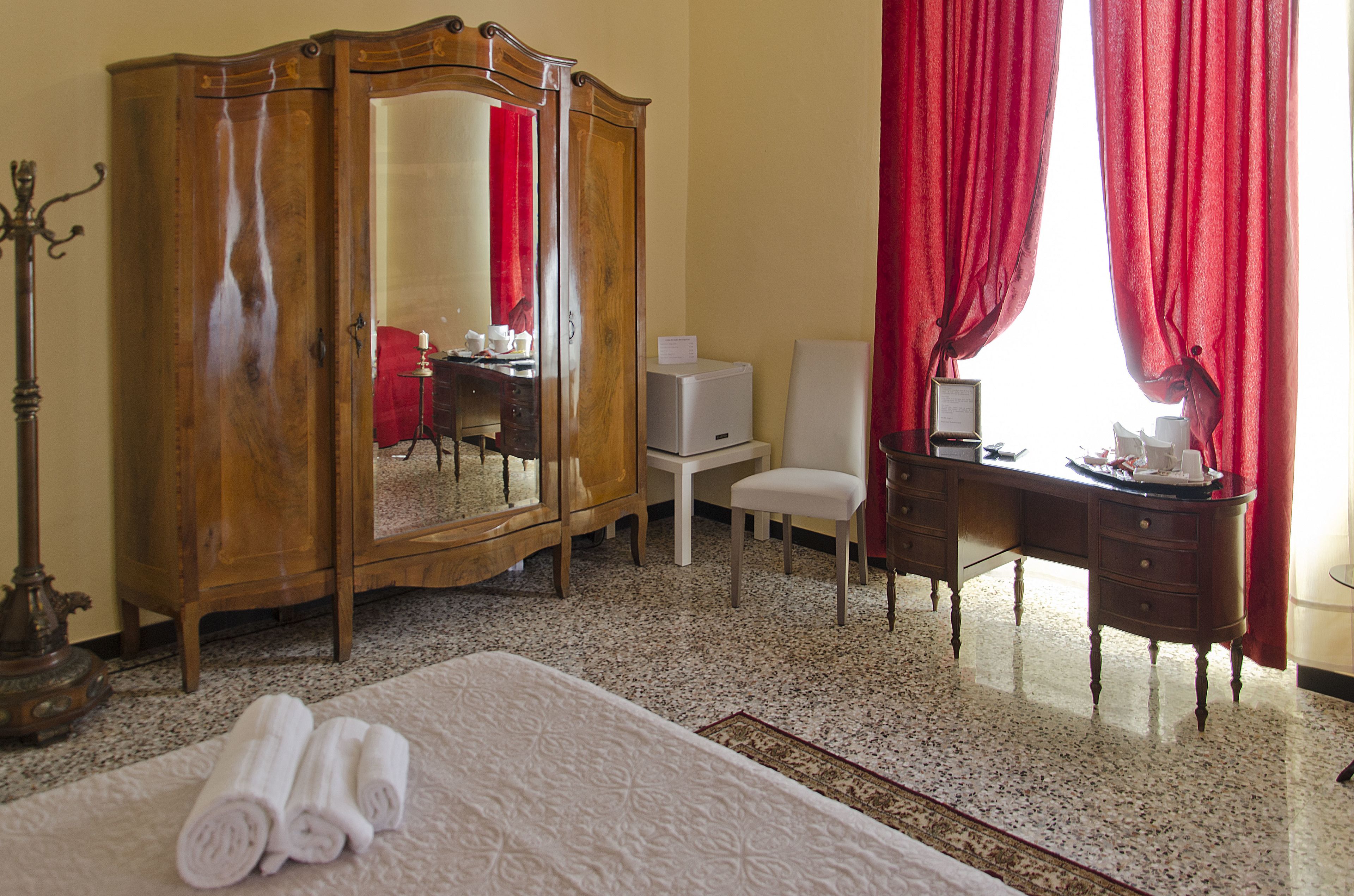 Une chambre d’hôtel avec un lit, une armoire en bois, un bureau avec une chaise, une petite table et un rideau rouge.