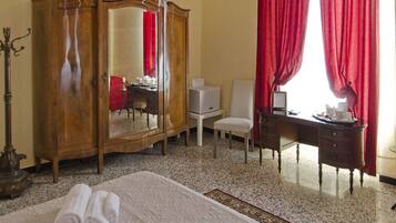 Une chambre d’hôtel avec un lit, une armoire en bois, un bureau avec une chaise, une petite table et un rideau rouge.