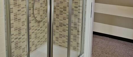 Una ducha con cerramiento de vidrio, pared con azulejos y una toalla blanca colgada en la puerta.