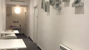 A modern interior with a long hallway, white walls, and a radiator. There are several white tables and chairs along the hallway. - Affittacamere Angel 2 (La Spezia)