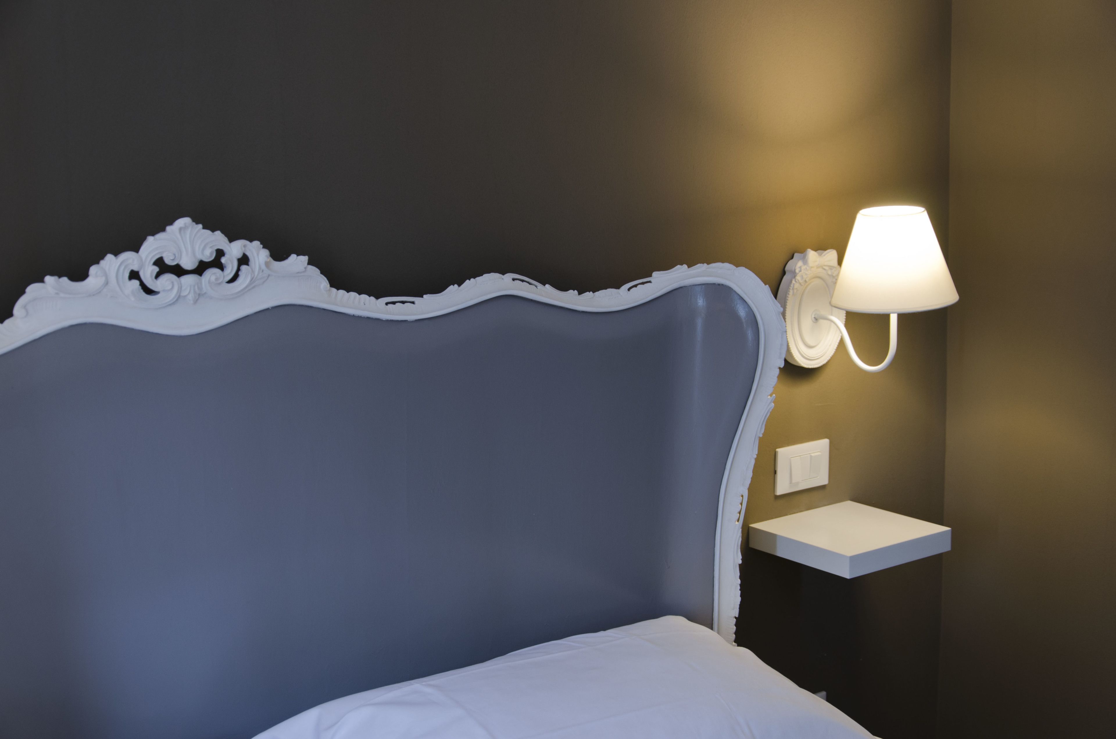 Ein Bett mit weißem Kopfteil und einem Nachttisch mit Wandlampe.