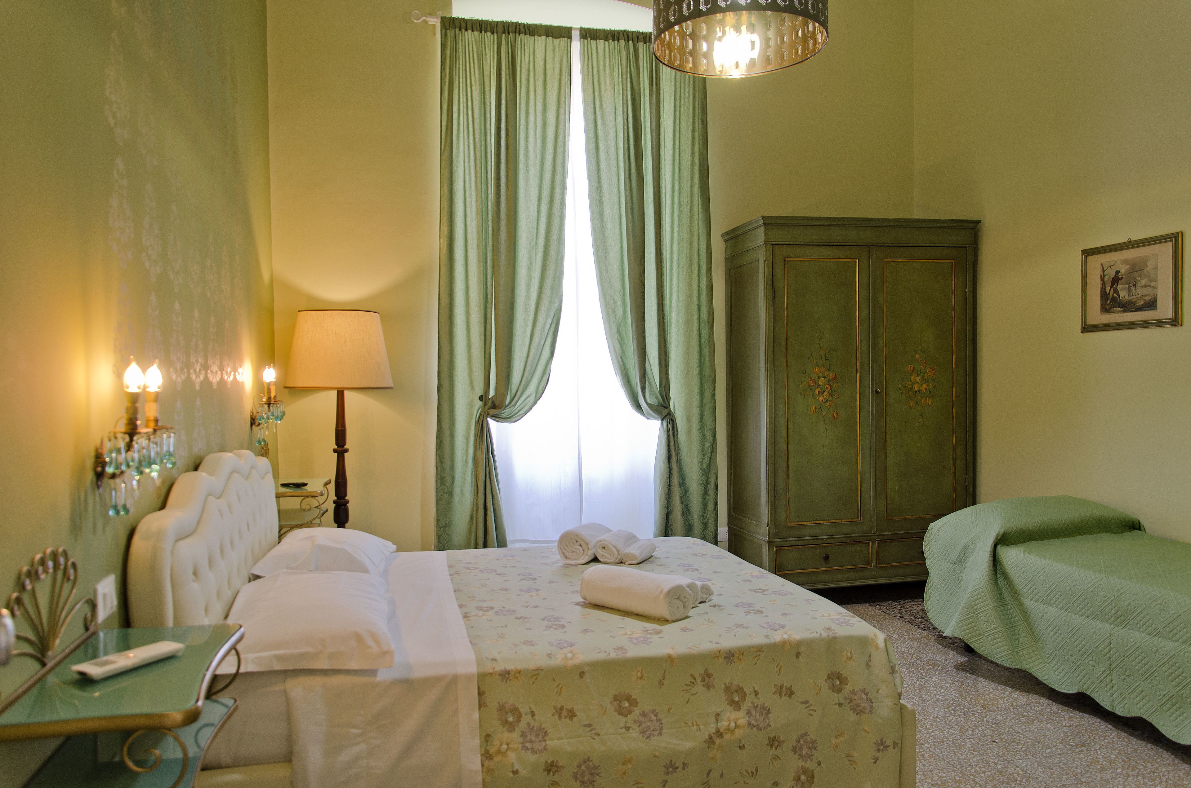 A hotel room with a bed, a green cabinet, a bedside table, and a lamp.