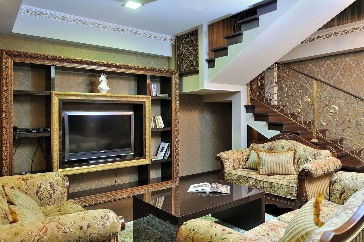 A living room with a large flat-screen TV, ornate furniture, and a staircase.