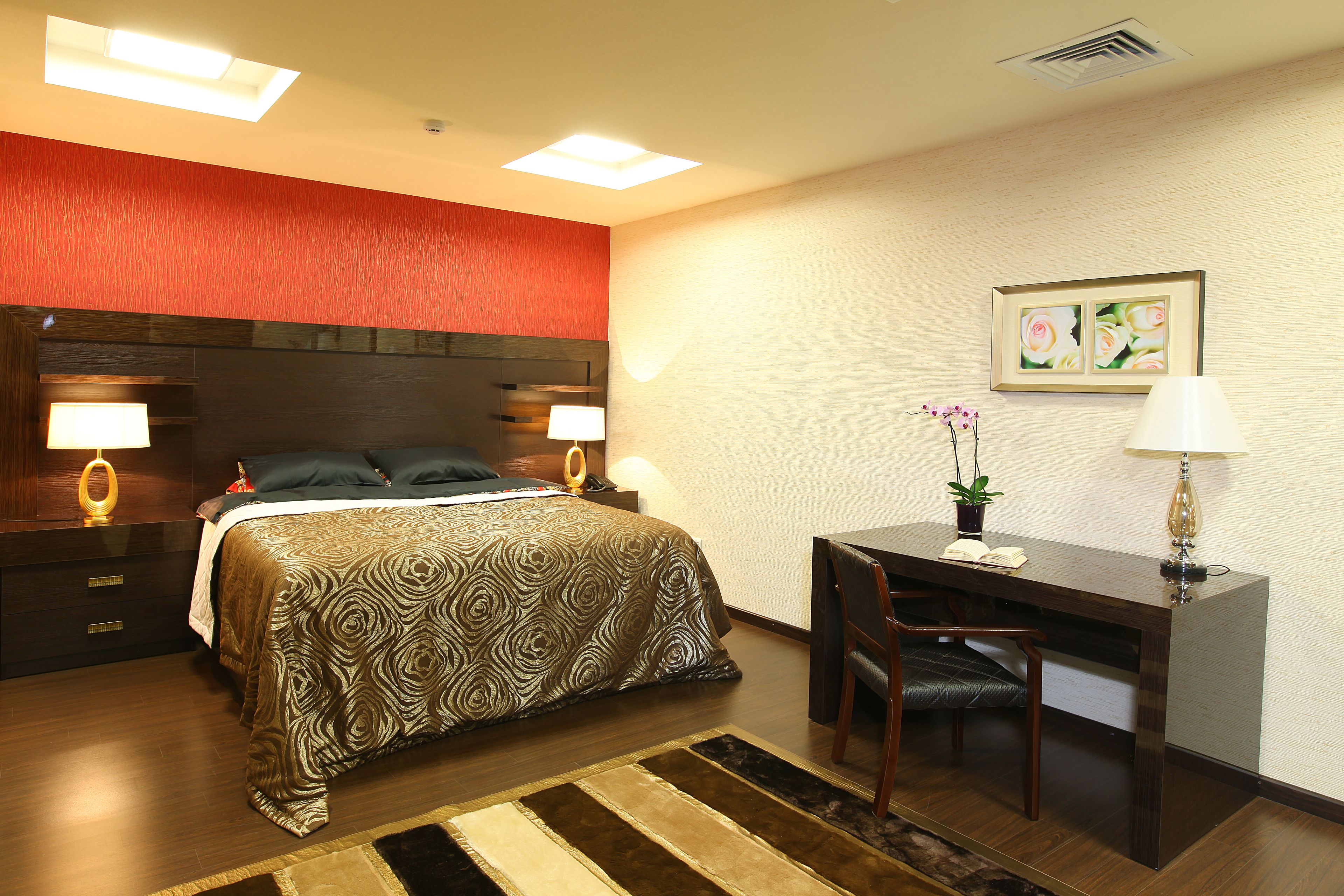 A hotel room with a bed, desk, chair, lamps, and a framed picture on the wall.