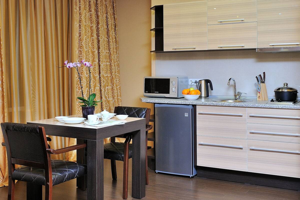 A compact kitchen with a dining area, featuring a microwave, kettle, and a small refrigerator.