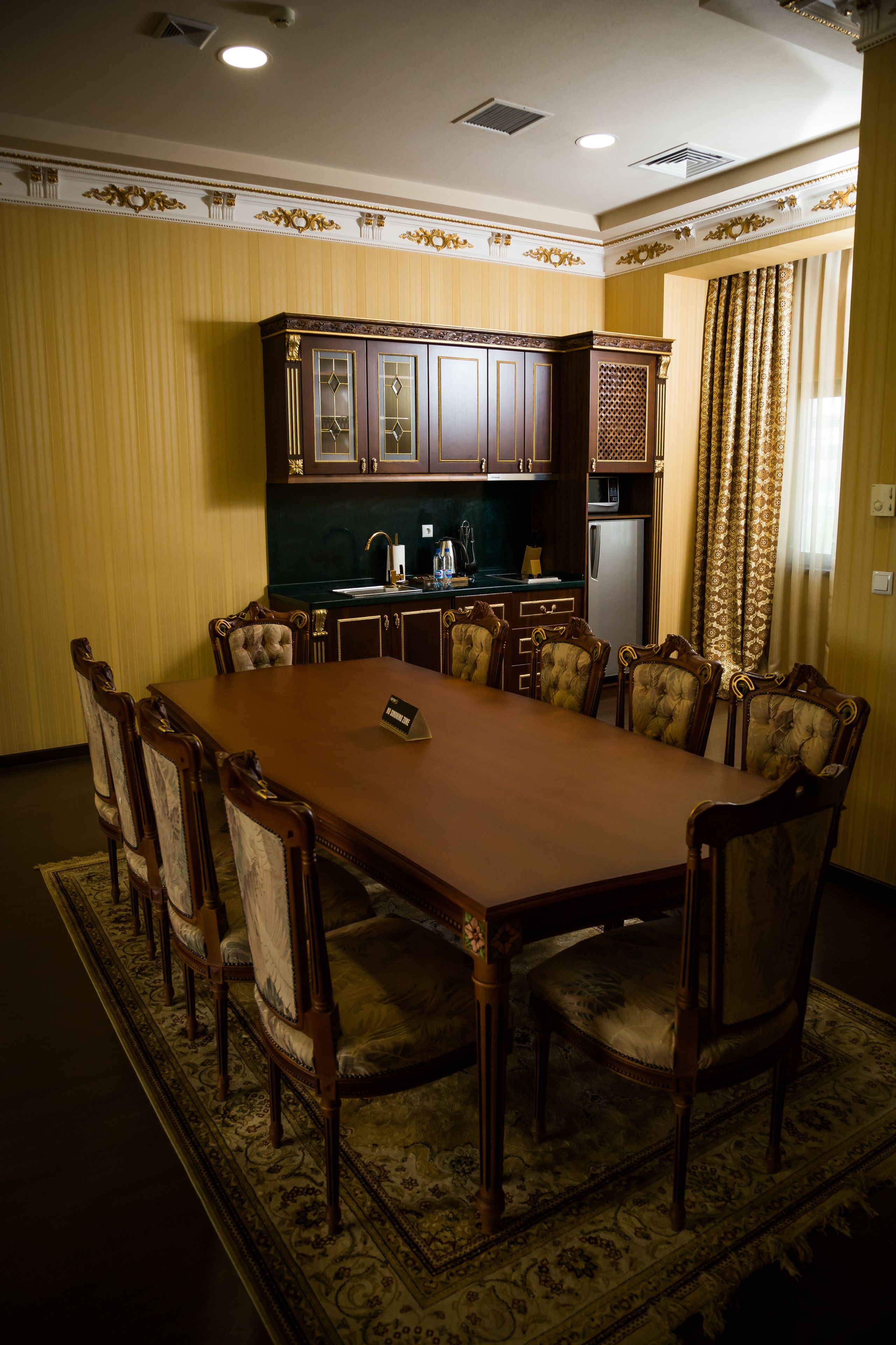 A conference room with a long table, eight chairs, and a kitchen area with cabinets and appliances.