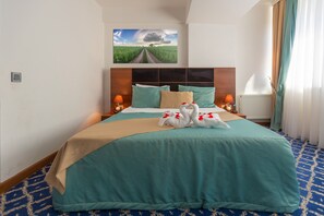 A hotel room with a large bed, a headboard with a built-in shelf, two bedside lamps, and a painting of a landscape above the bed. - Hotel 28 (Baku)