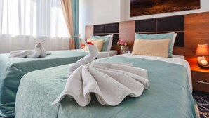A hotel room with two beds, each with a swan towel arrangement. There is a painting on the wall, a nightstand with a lamp, and a window with curtains. - Hotel 28 (Baku)