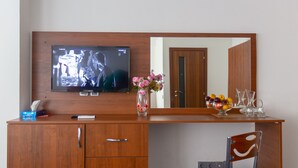 A hotel room with a wooden desk, a television, a vase with flowers, a fruit bowl, and a chair. - Hotel 28 (Baku)