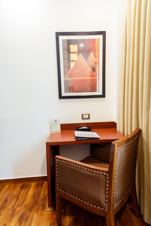 A small wooden desk with a chair, a framed picture on the wall, and a power outlet. - Ascent Biz Hotel (Noida)