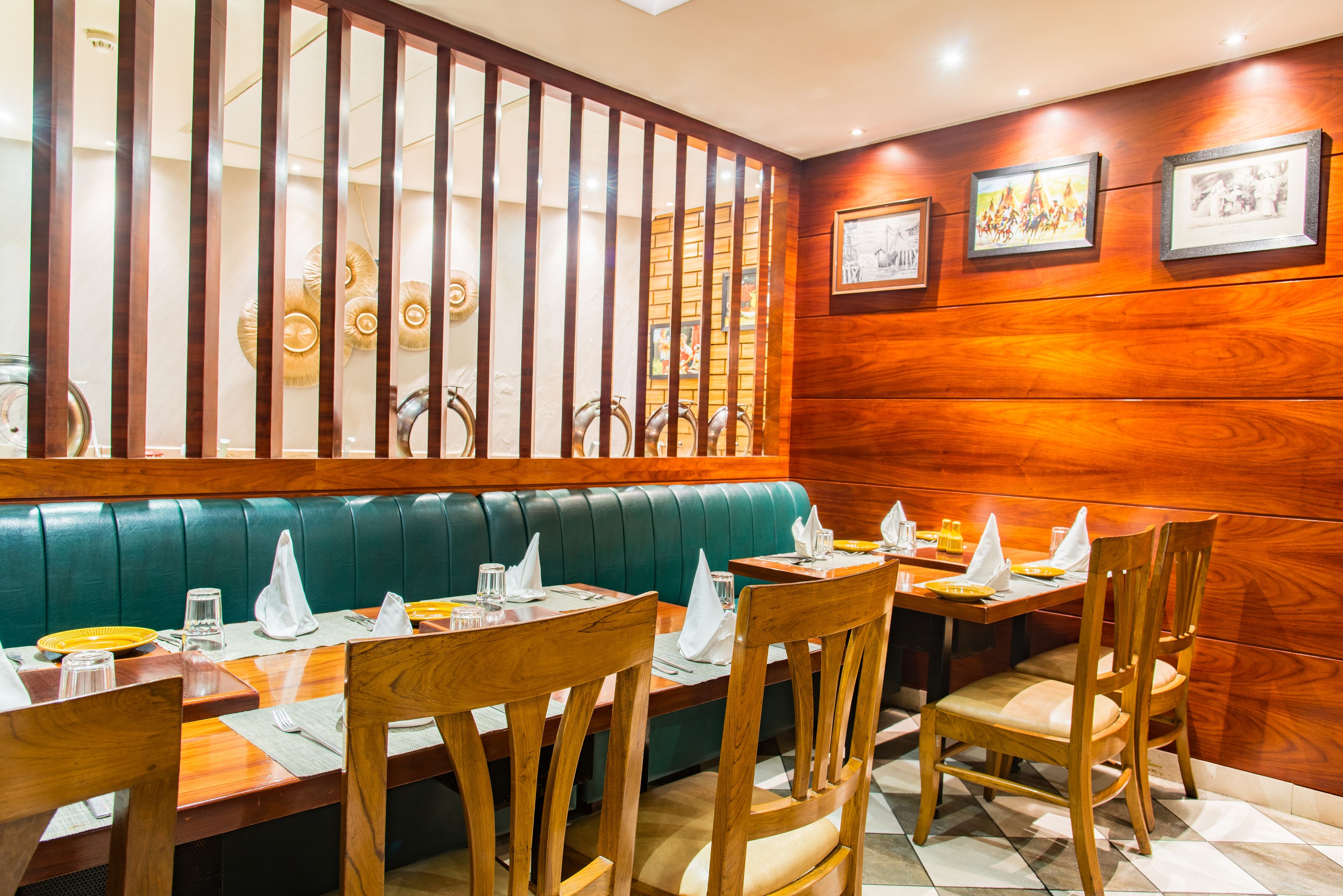 Un restaurante con mobiliario de madera, asientos acolchados verdes y cuadros en la pared.