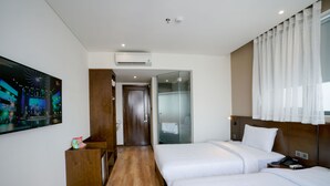 Habitación de hotel con dos camas, un escritorio de madera, un cuadro y cabina de ducha de vidrio.