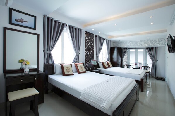 A hotel room with two beds, a desk, a chair, a TV, and a window with curtains.